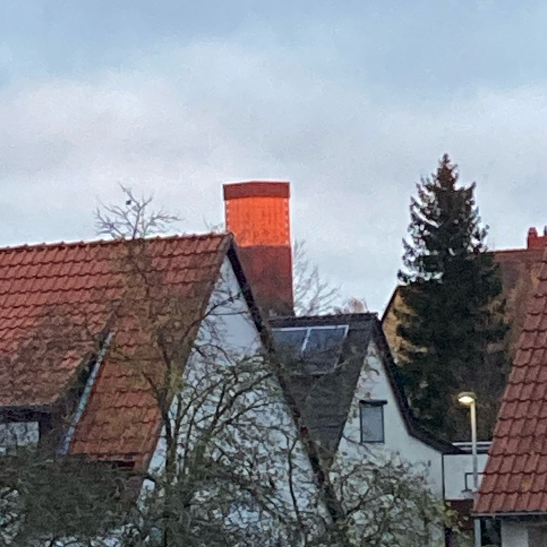 Kirchturm der Thomaskirche Wolfenbüttel im Morgenlicht hinter den noch im Schatten liegenden Dächern der umgebenden Wohnhäuser